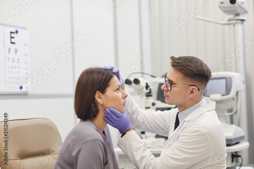 Side view portrait of young ophthalmologist opening eye of female patient while checking her vision in med clinic  copy space