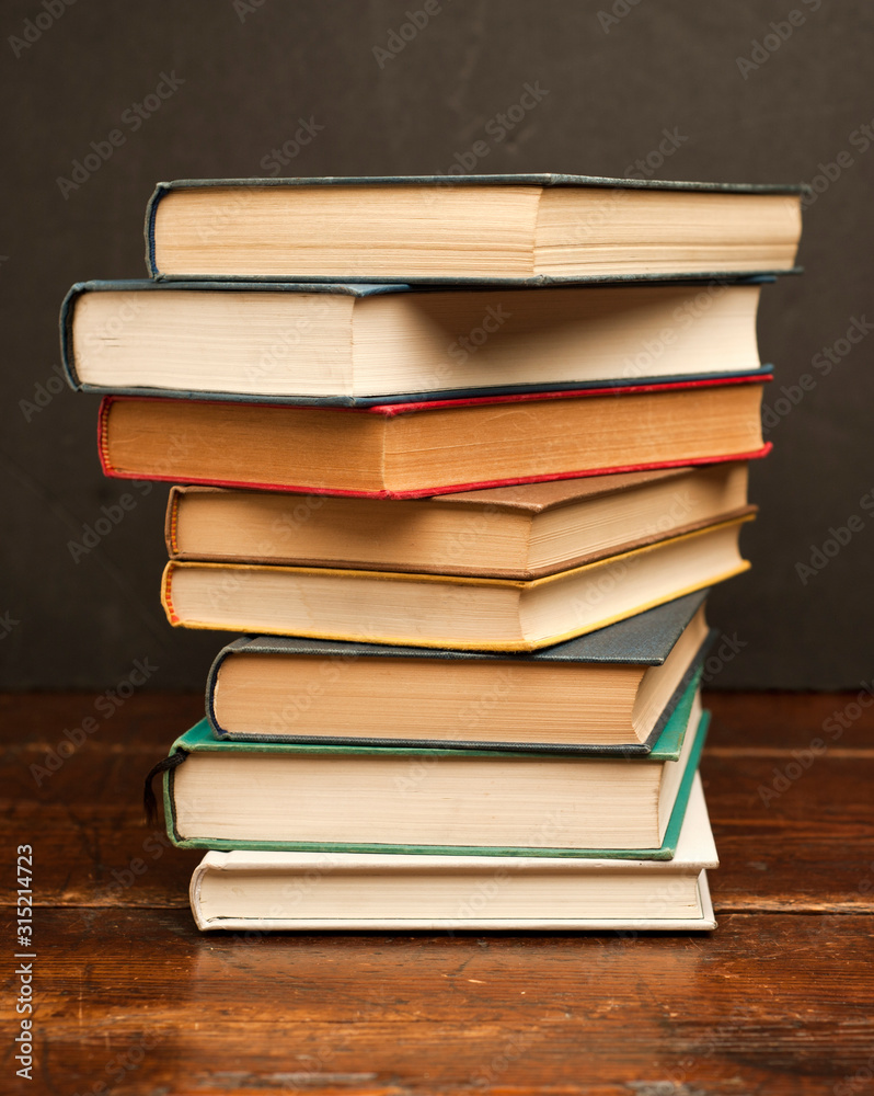 stack of colored books on old wooden shelf with dark background stack of colored books on old wooden shelf with dark background