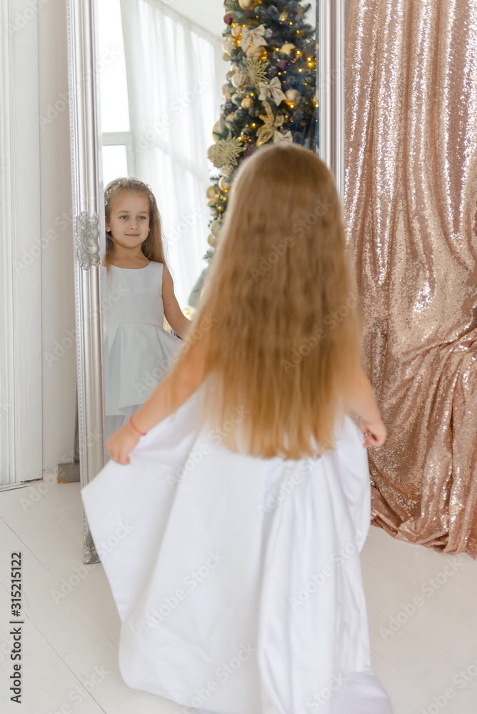 A little girl sits near a mirror and does a hairstyle before Christmas. A little girl sits near a mirror and does a hairstyle before Christmas.