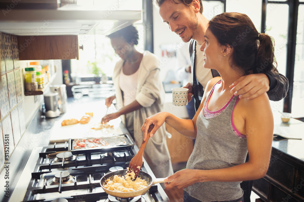 Young couple cooking scrambled eggs on stove in kitchen