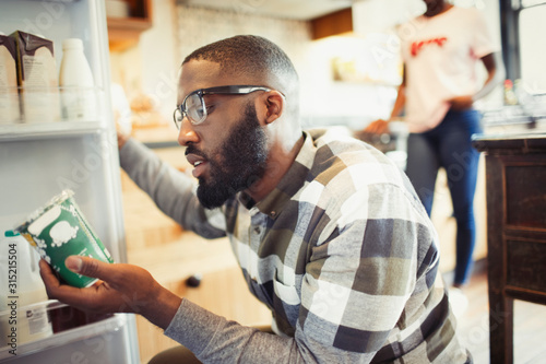 Young man reading label on container at refrigerator