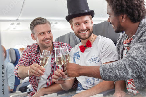 Young male friends toasting champagne glasses on airplane