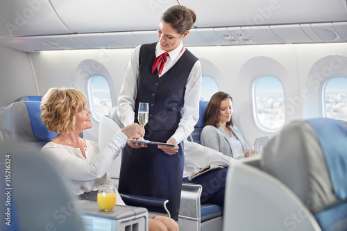 Flight attendant serving champagne to woman in first class on airplane photo
