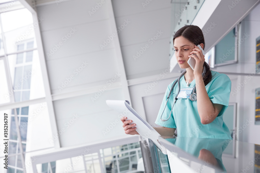 Female nurse with clipboard talking on cell phone in hospital Female nurse with clipboard talking on cell phone in hospital