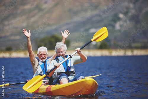 Playful, energetic active senior couple kayaking on sunny summer lake