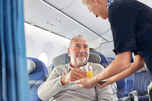 Flight attendant serving orange juice to man on airplane photo