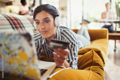 Young woman credit card headphones online shopping at laptop on living room sofa