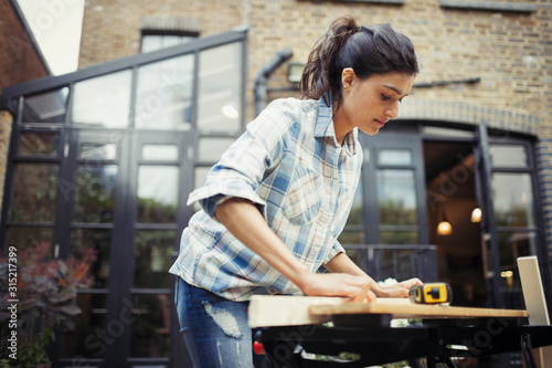 Young woman measuring wood on patio photo