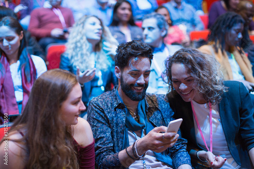Smiling business people using smart phone in conference audience