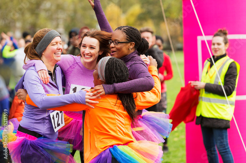Enthusiastic female runners in tutus hugging at finish line, celebrating photo