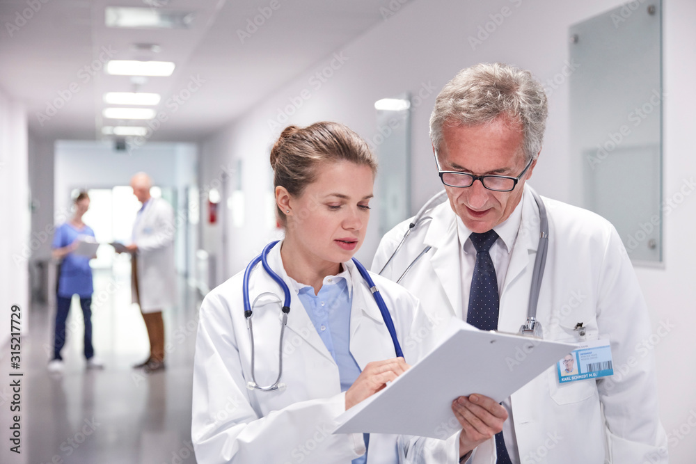 Doctors with clipboard making rounds, talking in hospital corridor