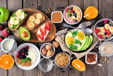 Healthy breakfast table scene with fruit, yogurts, oatmeal, smoothie, nutritious toasts and egg skillet. Top view over a wood background.