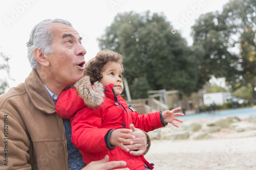 Grandfather and toddler grandson playing with bubbles in park
