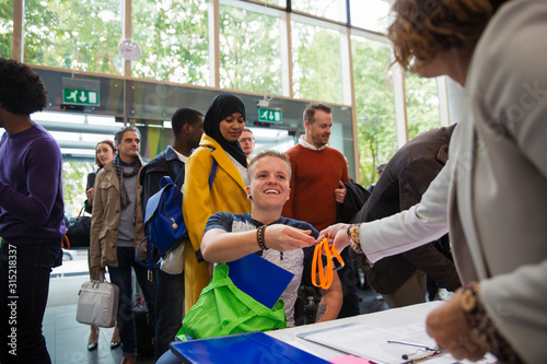 Smiling woman in wheelchair arriving checking in at conference registration table photo