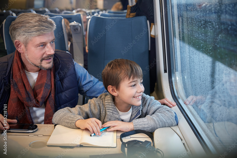 © Agnieszka Olek/Caia Image - Father and son looking out window on passenger train