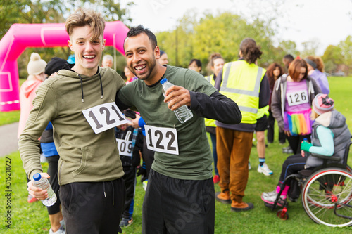 Portrait enthusiastic male runner friends water hugging at charity run finish line in park photo