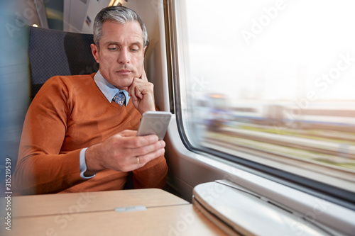 Focused businessman using smart phone at passenger train window photo