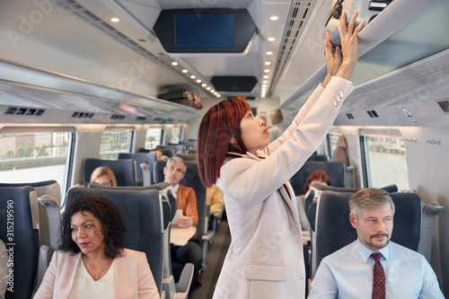 Businesswoman stowing suitcase in overhead compartment on passenger train photo