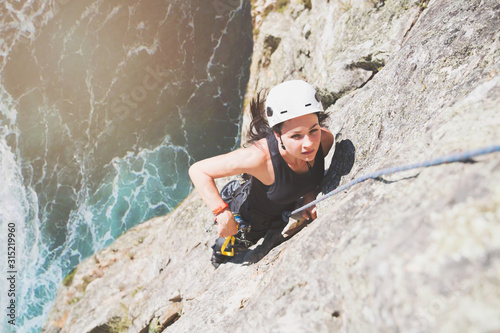 Focused, determined female rock climber scaling rock above sunny ocean