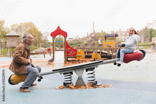 Grandfather and granddaughter playing on seesaw at playground
