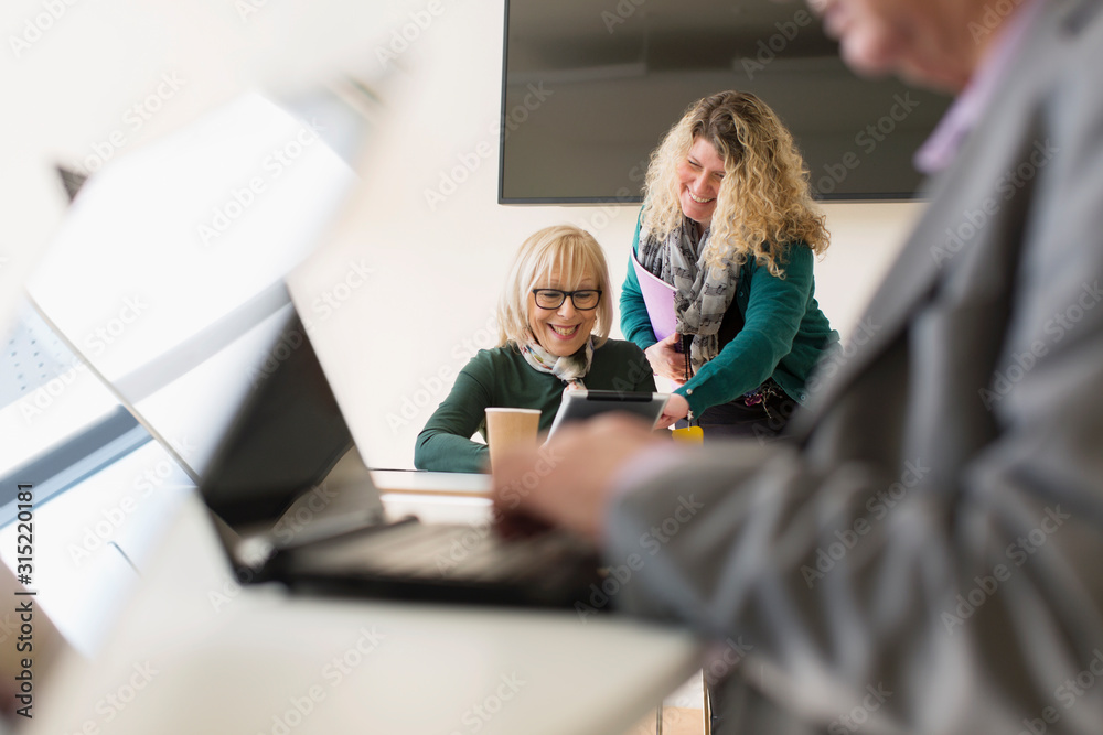 © Martin Barraud/Caia Image - Businesswomen using digital tablet in conference room meeting