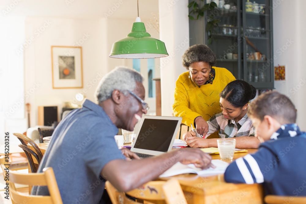 Grandparents helping grandchildren with homework at dining table