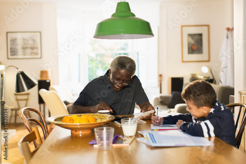Grandfather at dining table with grandson doing homework
