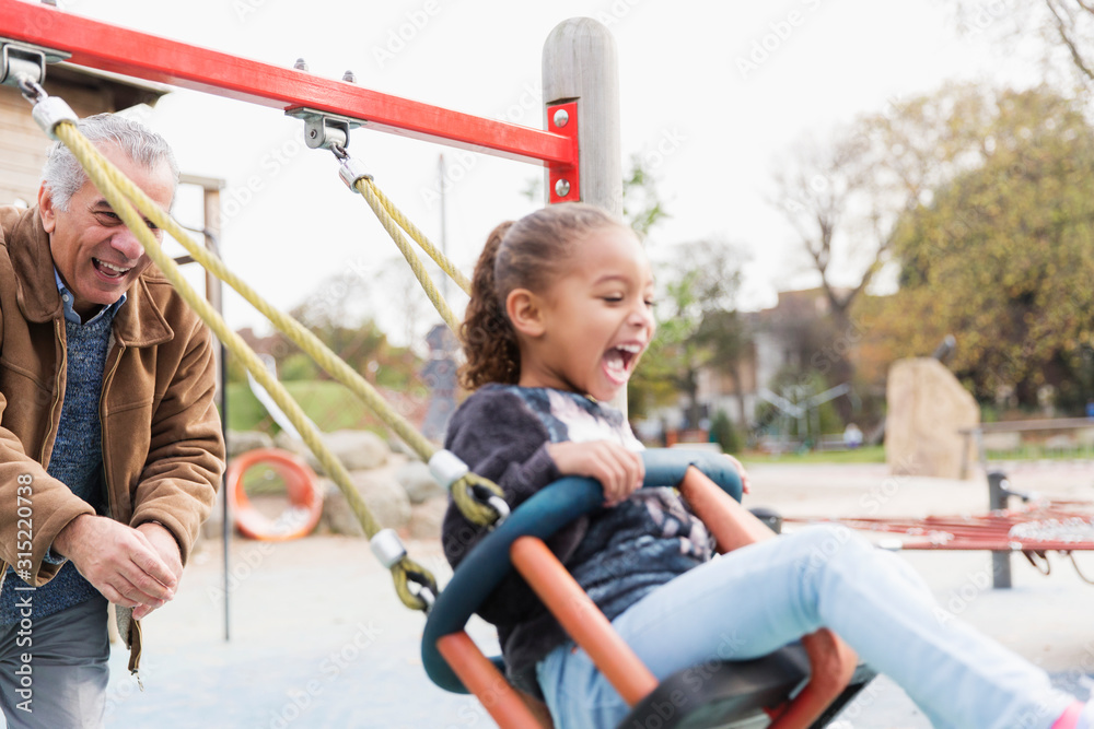 Playful grandfather pushing granddaughter on playground swing Playful grandfather pushing granddaughter on playground swing