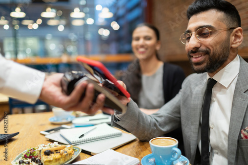 Businessman paying with smart phone contactless payment in cafe photo