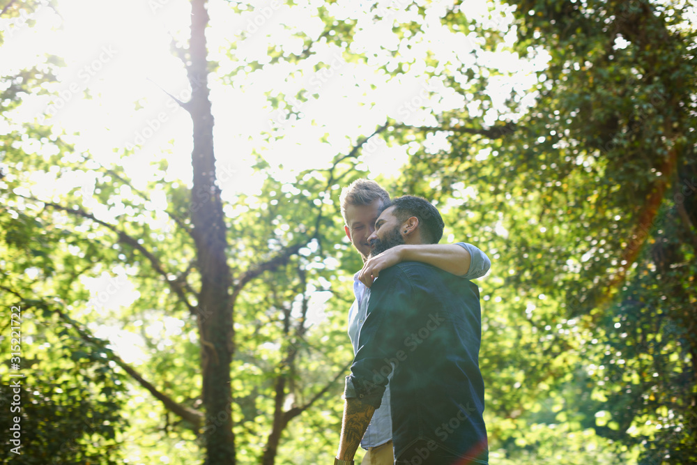 Affectionate gay couple hugging and walking in sunny park Affectionate gay couple hugging and walking in sunny park