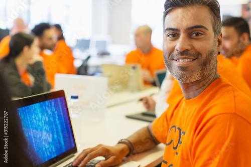 Portrait confident hacker at laptop coding for charity at hackathon photo