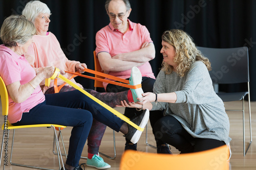 Instructor helping active seniors stretching legs, exercising straps
