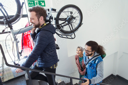 Friends carrying bicycle up stairwell