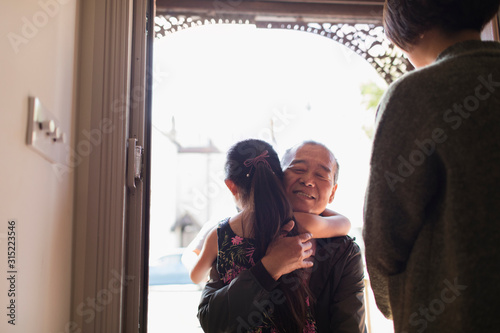 Affectionate granddaughter greeting and hugging grandfather in doorway