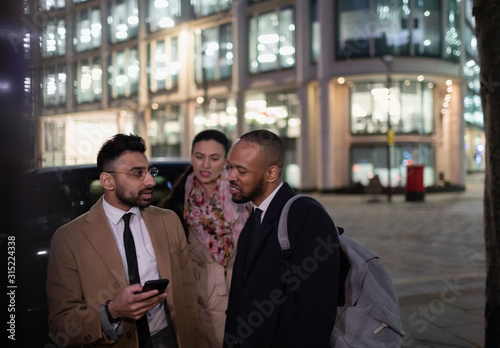 Business people with smart phone talking on city street at night photo
