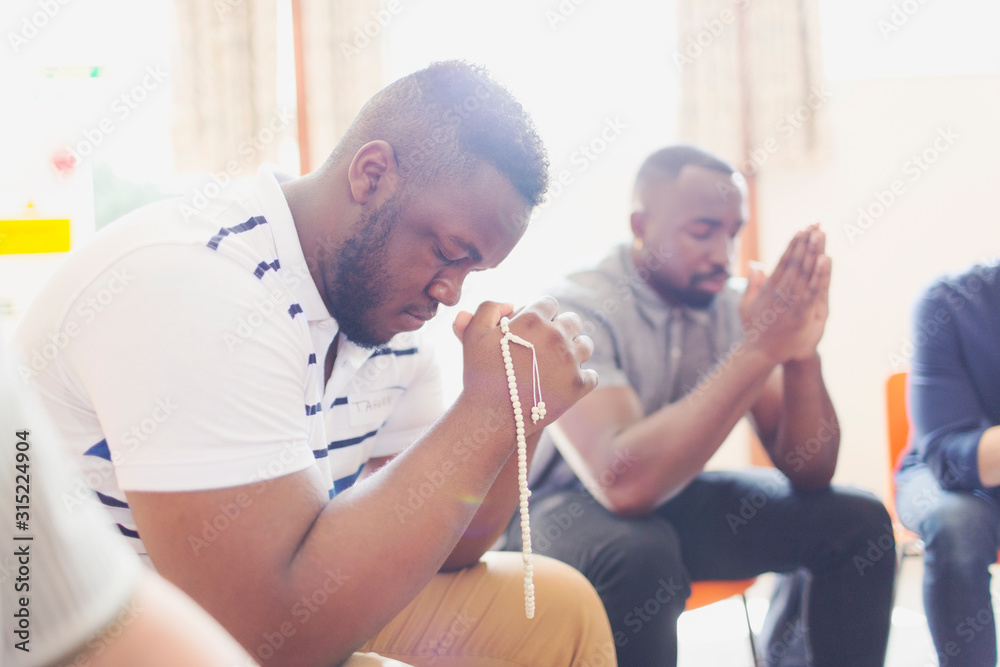 Man praying with prayer beads in prayer group Man praying with prayer beads in prayer group