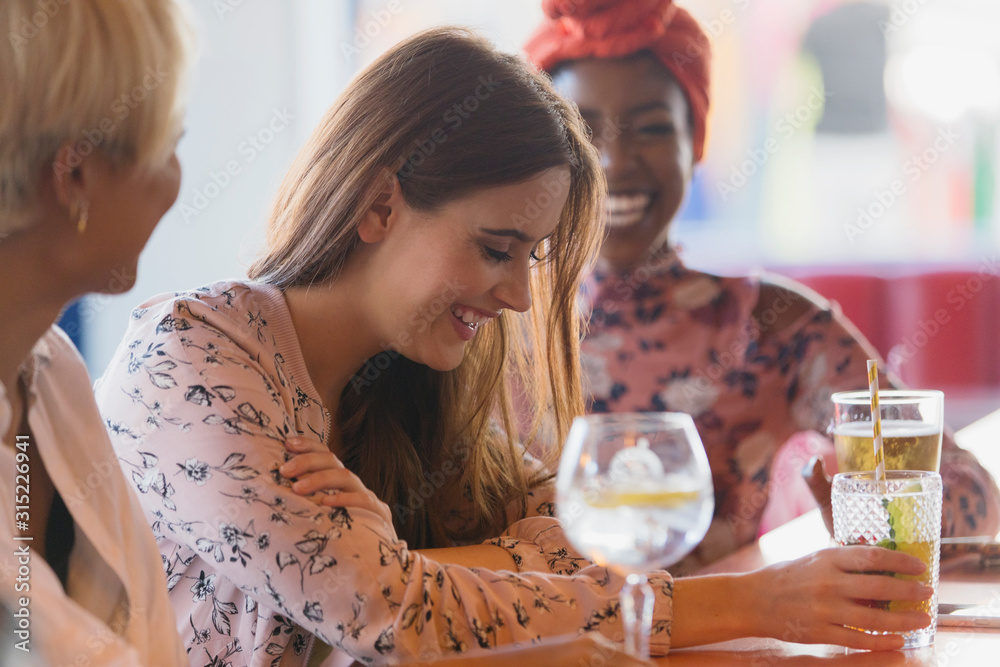 Young women friends laughing, drinking cocktails in bar