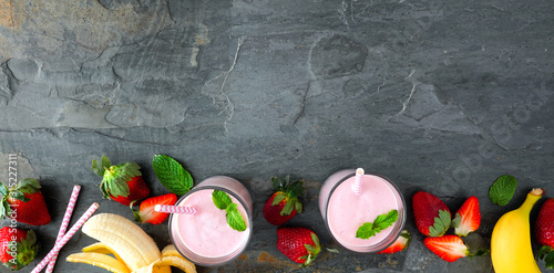 Banner with healthy strawberry banana smoothie bottom border. Top view over a dark stone background. Copy space.