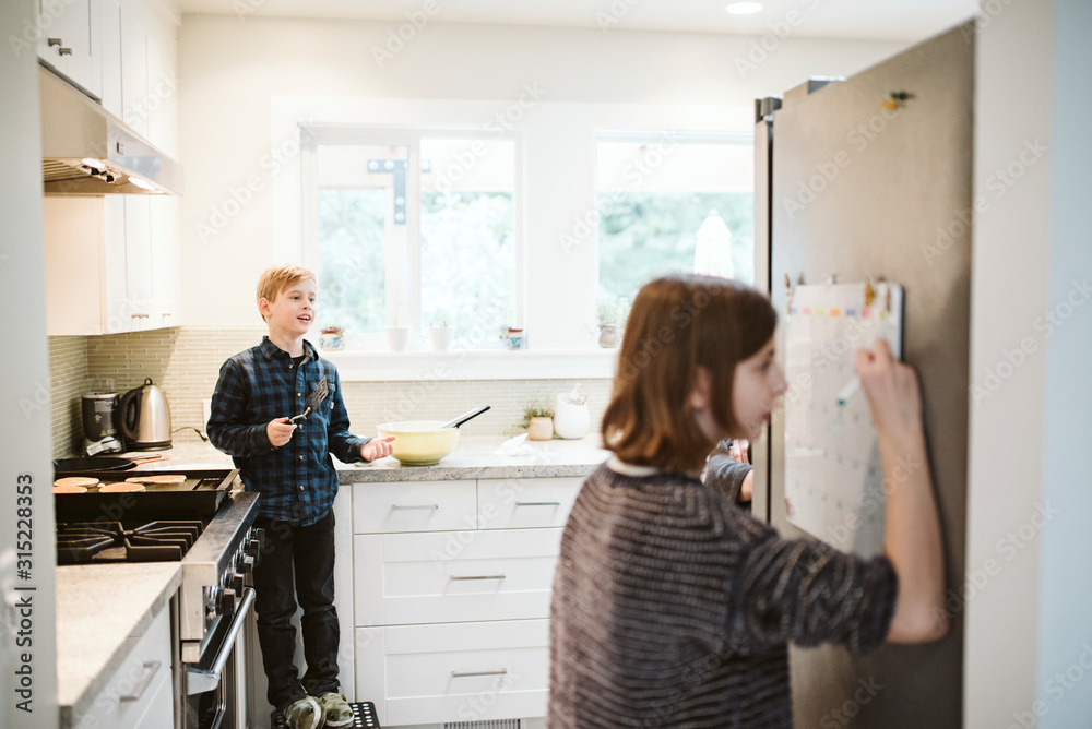 Brother and sister cooking and writing on calendar in kitchen Brother and sister cooking and writing on calendar in kitchen