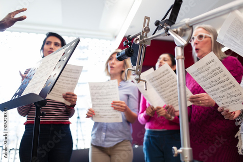 Womens choir with sheet music singing in music recording studio