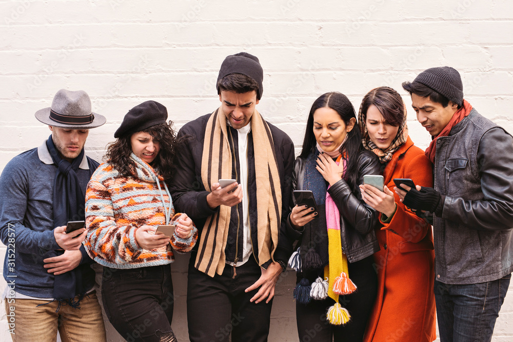 Fototapeta premium Young friends look in disgust at their smart phones - Diversity - Dressed in Winter Clothing in the daytime
