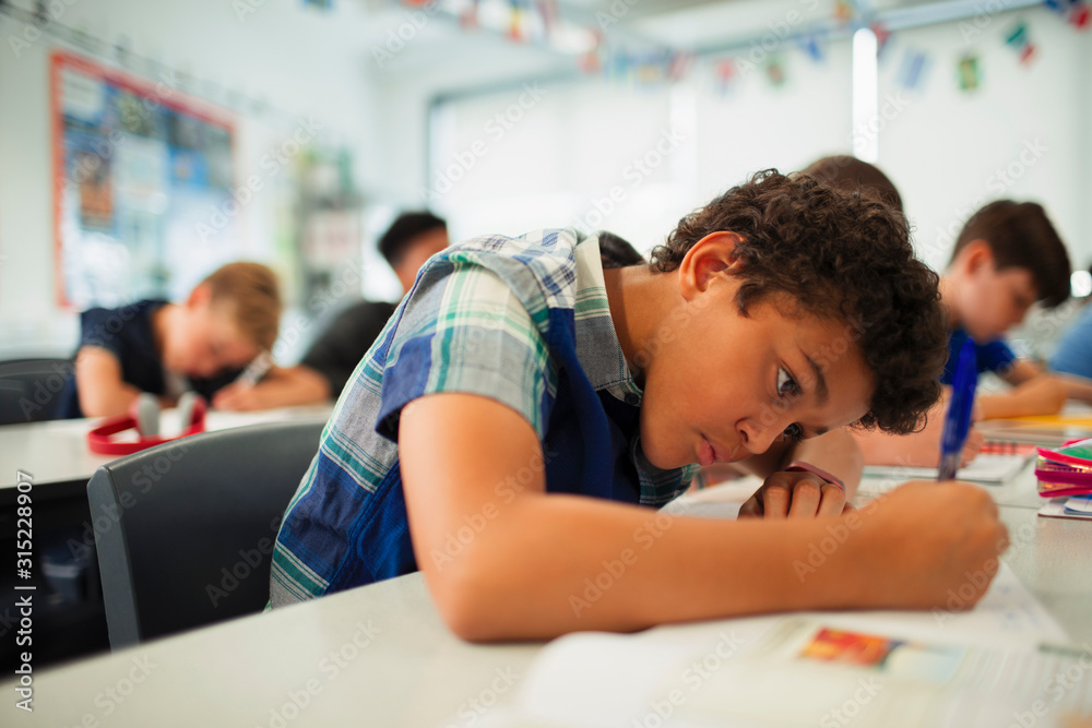 Focused junior high school boy doing homework in classroom Focused junior high school boy doing homework in classroom