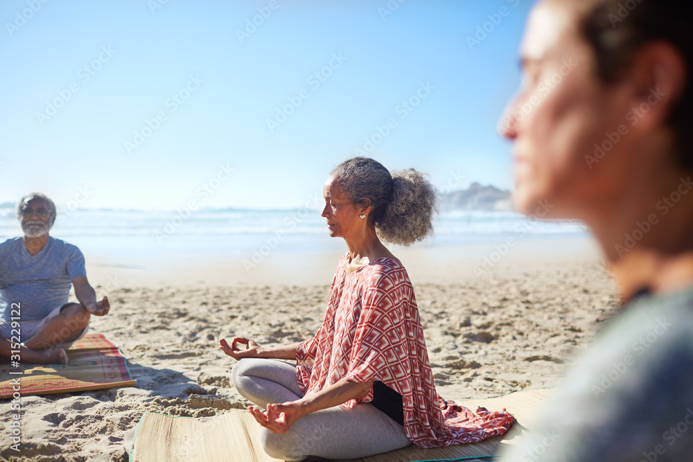 Serene senior woman meditating on sunny beach during yoga retreat Serene senior woman meditating on sunny beach during yoga retreat