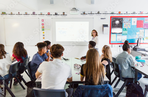 High school students watching female teacher leading lesson at projection screen in classroom photo