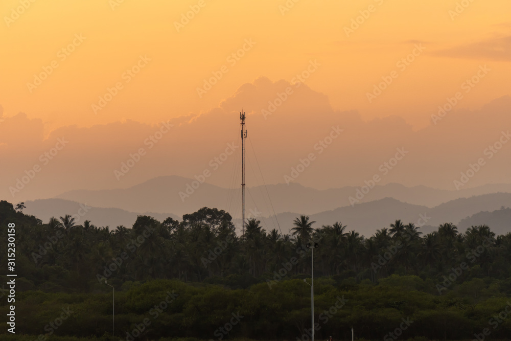 Beautiful sunset scenic of moutain and coconut woods in suburb of Thailand with telecommunication pole in the middle of the photo.