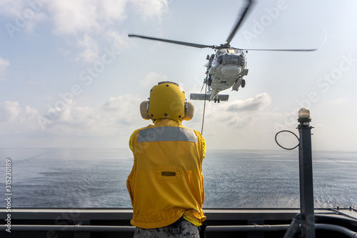 Fotografija Helicopter deck officer give hand signal to Sikorsky S-70 Sea Hawk helicopter hovering above helicopter deck of Navy ship to perform hot refueling while flying at sea