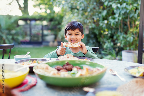 Portrait happy boy eating naan bread at patio table photo