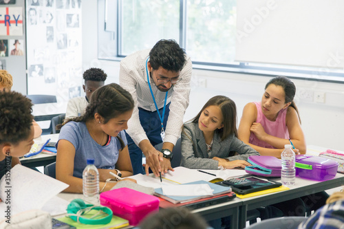 Male teacher helping junior high school girl students at desk in classroom photo