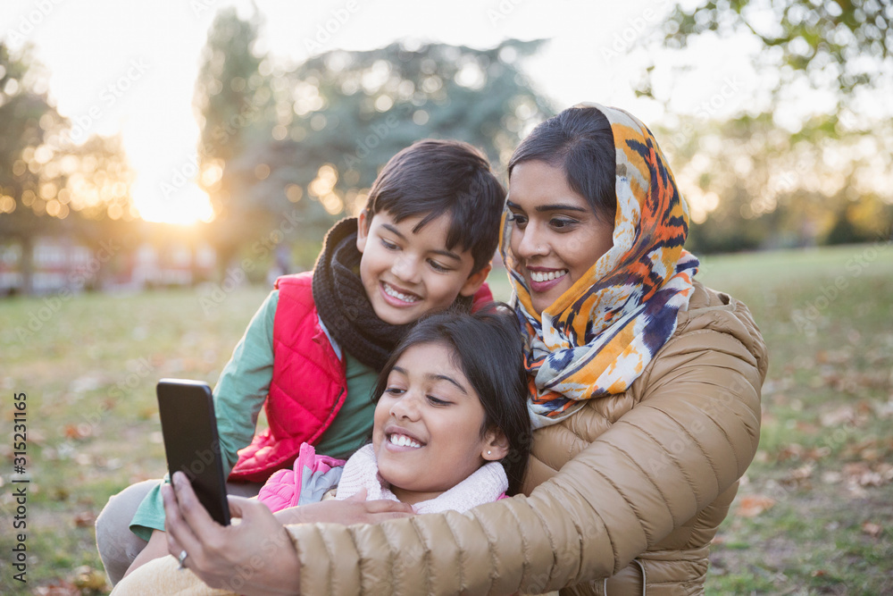 Muslim mother in hijab taking selfie with camera phone in autumn park Muslim mother in hijab taking selfie with camera phone in autumn park