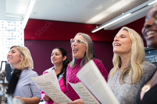 Womens choir with sheet music singing in music recording studio